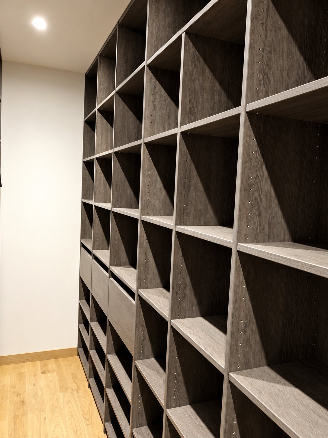 Grand meuble de rangement sur mesure en bois foncé, avec de nombreuses étagères et quelques tiroirs, dans une pièce aux murs blancs et au parquet clair.